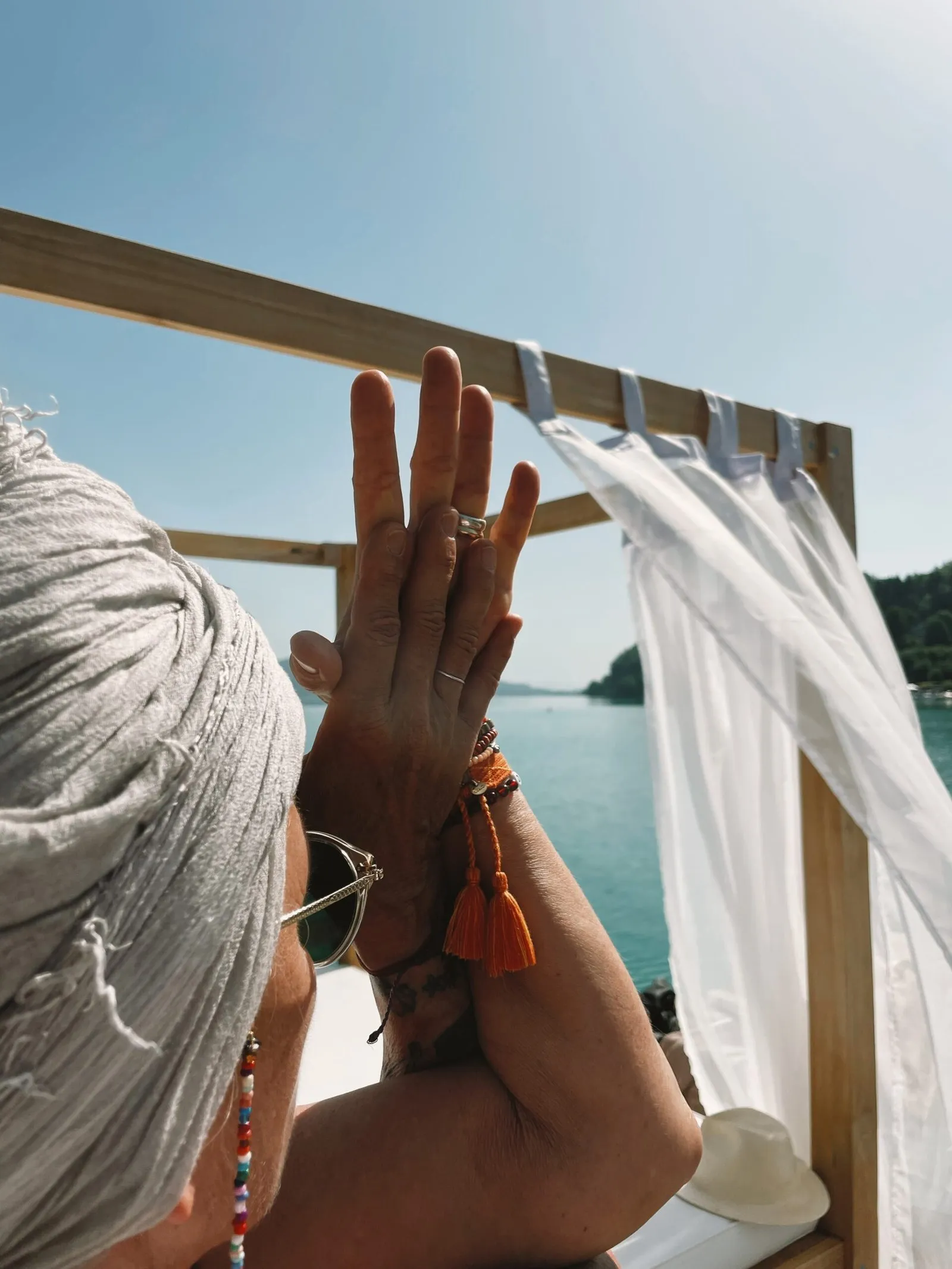 Frau mit Turban legt die Handflächen vor einem Holzrahmen mit weißem Vorhang am See aneinander