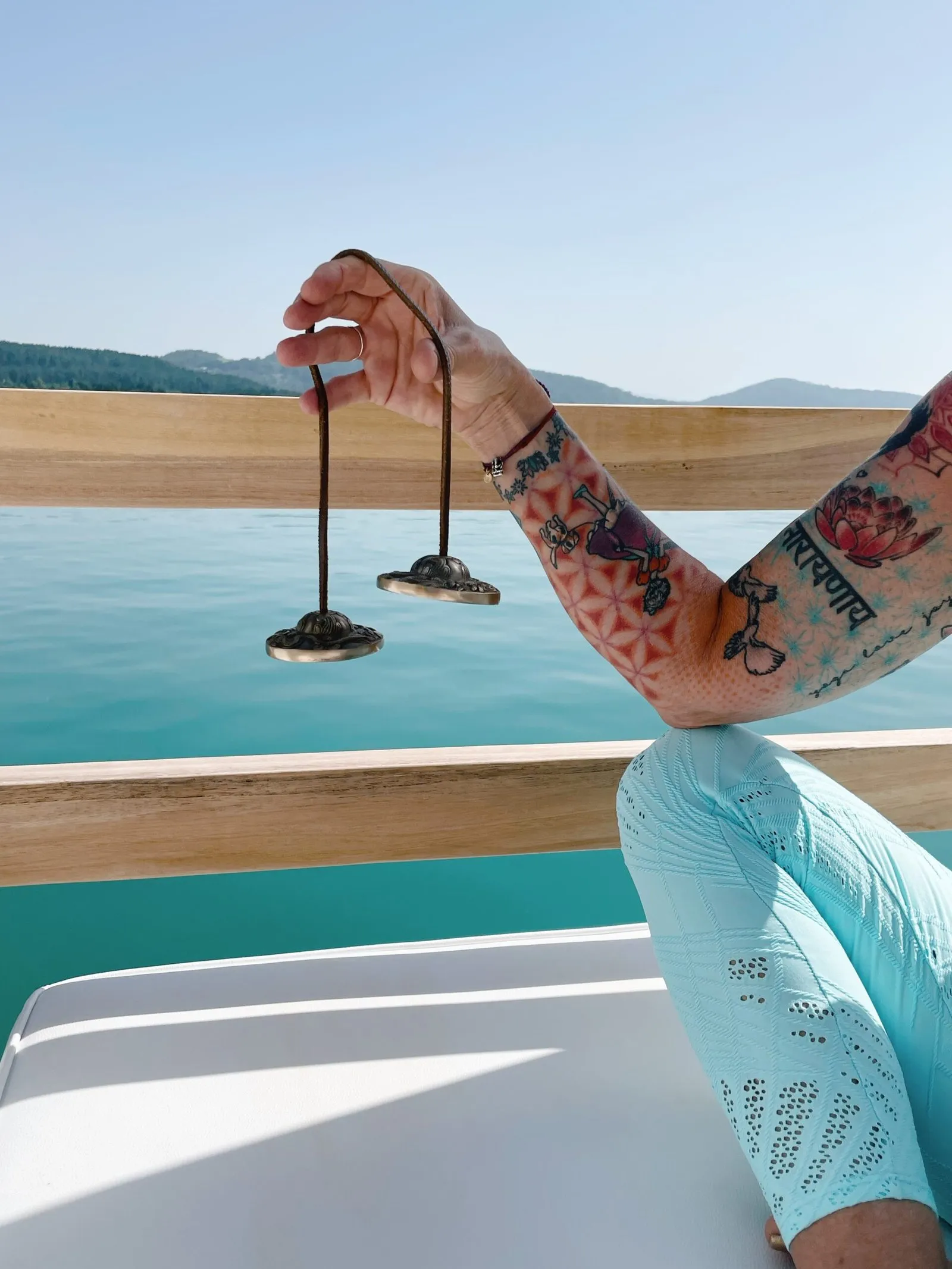 Hand hält tibetische Zimbeln über der Reling eines Bootes am See